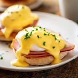 A close-up of Eggs Benedict, featuring a perfectly runny yolk, crisp bacon edge, and buttery English muffin.