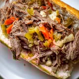 Close-up of a Chicago-style Italian Beef Sandwich overflowing with juicy shredded beef and giardiniera, served alongside a small bowl of rich au jus.