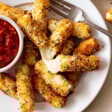Crispy panko-crusted mozzarella sticks arranged neatly with a bowl of warm red dipping sauce.