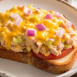 Freshly broiled Tuna Melt on whole wheat toast, showcasing creamy tuna salad, melted Swiss cheese, and a side of crisp dill pickles.