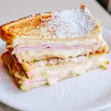 A perfectly fried Monte Cristo sandwich, layered with melted Swiss cheese and ham, ready to be dipped in sweet jam. 