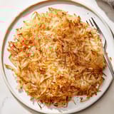 Freshly grated hash browns topped with chives, served alongside sunny-side-up eggs.