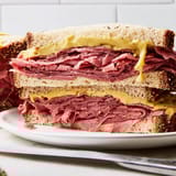 Close-up of a Pastrami on Rye deli sandwich with pickles, showcasing the layered meat between fresh bread slices.