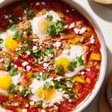 Shakshuka topped with cilantro and feta, served alongside crusty bread for dipping.