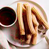 Freshly fried Spanish churros with crisp edges and soft centers, served warm on a white plate.