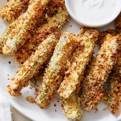 Homemade Fried Pickles spears with seasoned breadcrumbs and creamy ranch dip on a wooden serving board.