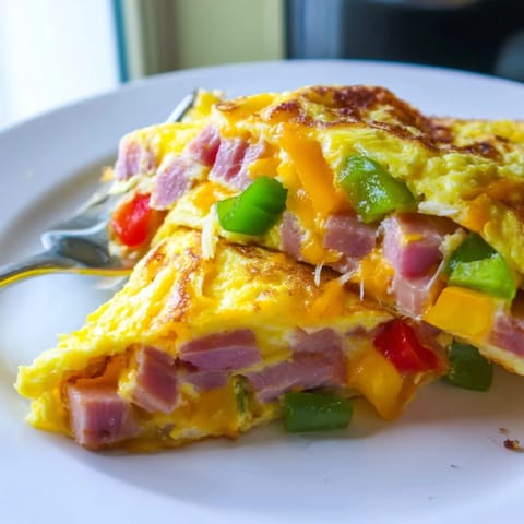 Denver Omelet folded in half with melted cheddar, filled with diced ham, sautéed bell peppers, and onions on a white plate.
