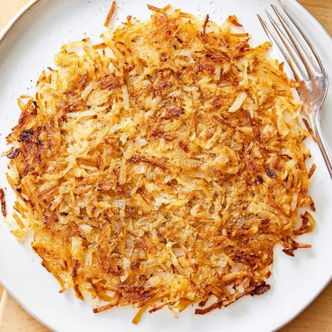 Golden brown shredded hash browns sizzling in a skillet, perfectly crispy for breakfast.