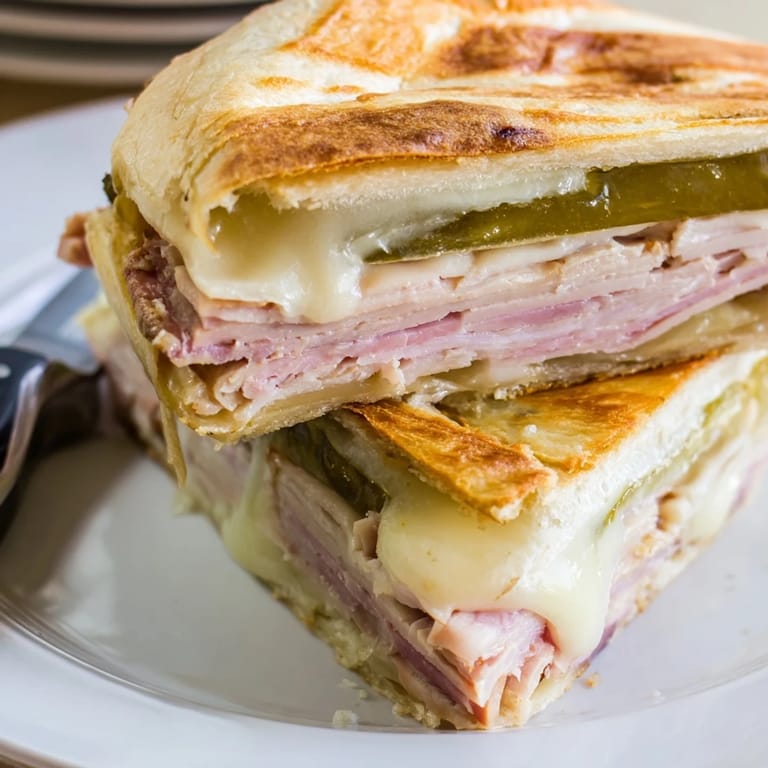 A freshly sliced Cuban sandwich showcases juicy roast pork, ham, and mustard, paired with plantain chips for a Cuban meal.