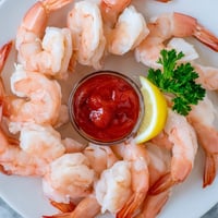 Chilled pink Shrimp Cocktail arranged on a bed of crushed ice with lemon wedges and zesty sauce.