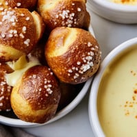 Golden-brown pretzel bites with a bowl of creamy, melted cheese dip on a rustic wooden table.