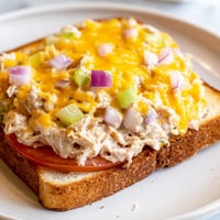 Golden-brown Tuna Melt sandwich on sourdough bread, with bubbling cheddar cheese and a slice of ripe tomato, served on a plate.