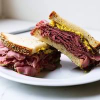 Freshly assembled Pastrami on Rye sandwich stacked high with warm, juicy meat and yellow mustard on crusty rye.
