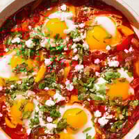 Steaming shakshuka in a cast iron skillet with poached eggs in rich tomato sauce.